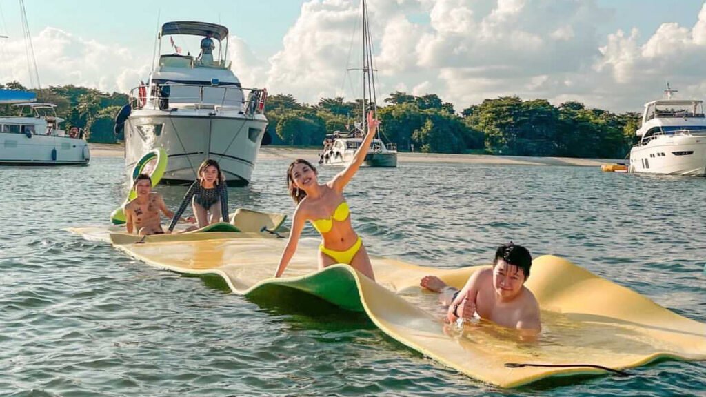 A group of young people lounging on water mats next to Mikanna yacht